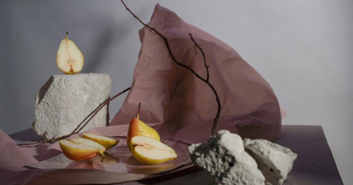 Minimal still life of pears, paper, stones, and branches arranged like raw materials becoming a structured composition.