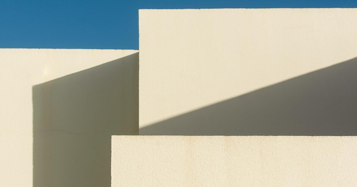 Abstract white building walls and geometric shadows under a blue sky, suggesting infrastructure and workflow layers.